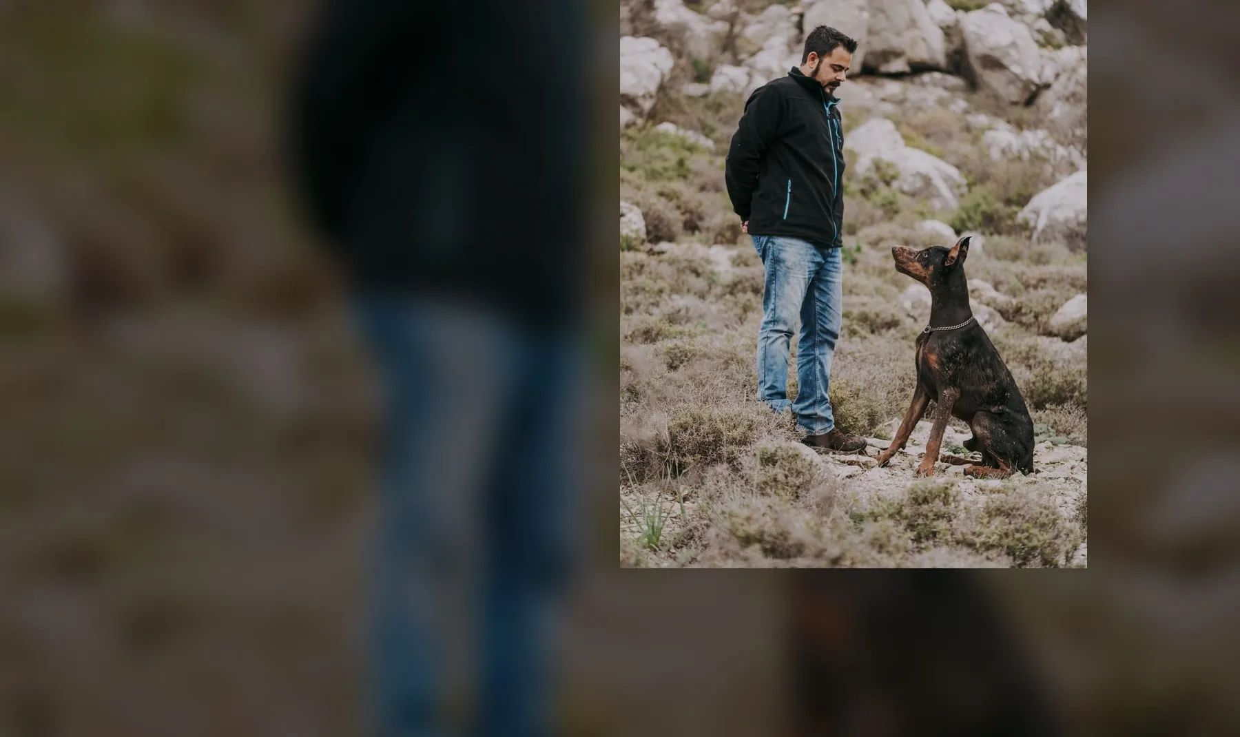 Mann steht neben einem Dobermann in felsiger Landschaft